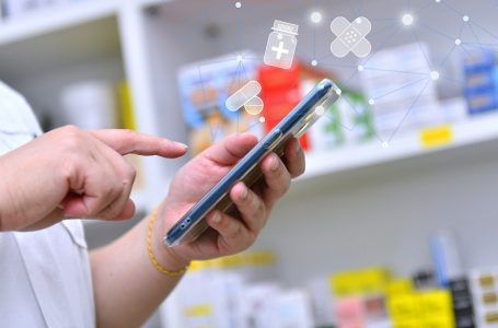 Pharmacist holding mobile phone using for filling prescription in pharmacy drugstore